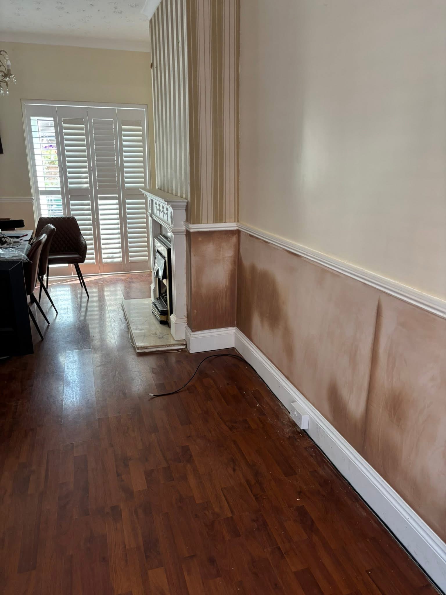 A dining room with fresh plaster along the lower walls and chimney breast, wood floor and shutters