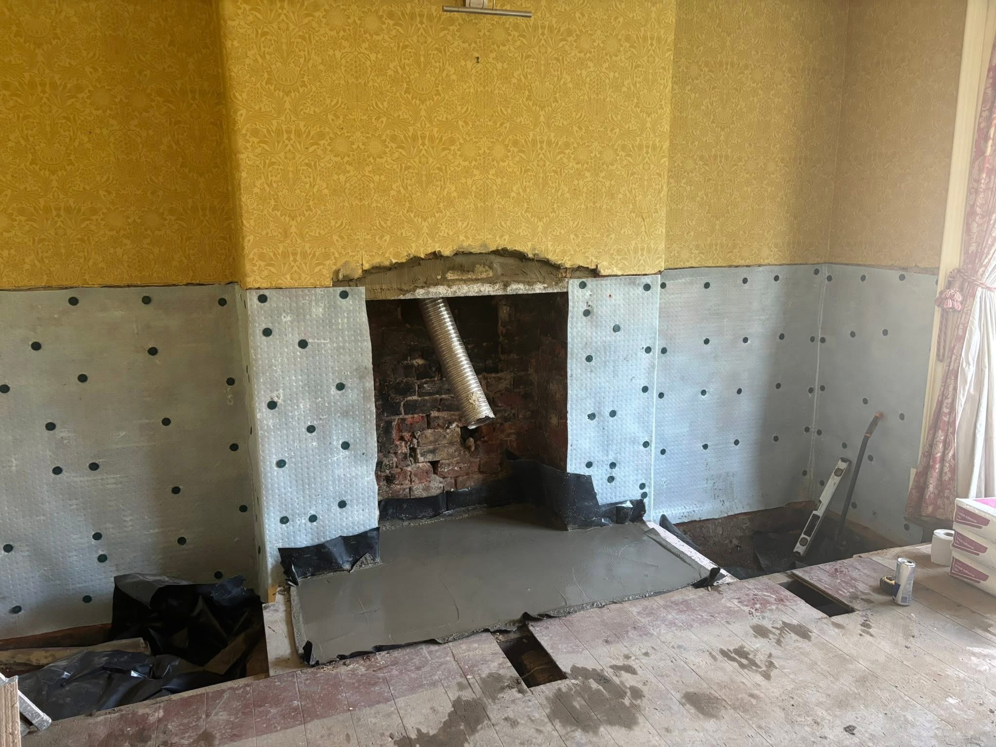 Lower walls covered in studded damp membrane around a chimney breast, with a new concrete hearth laid